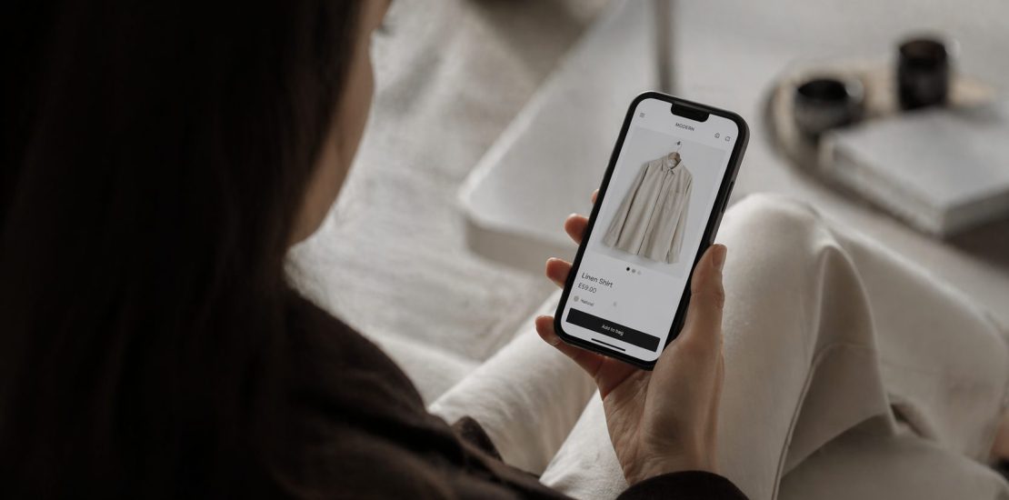 Person holding a smartphone displaying an online clothing product page for a linen shirt.